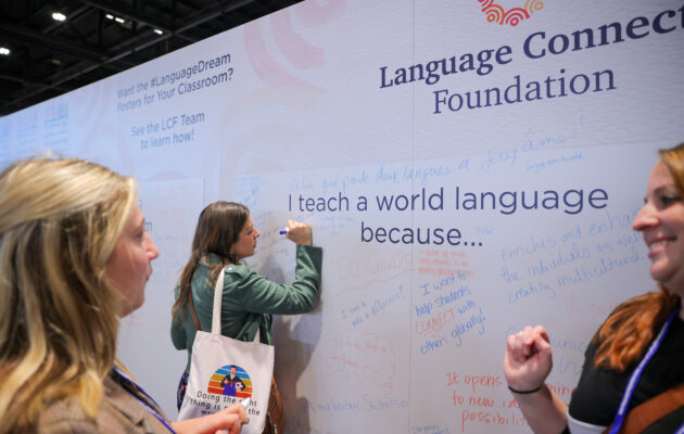 Two women in the foreground talk while a third writes on the Inspiration Wall with a marker