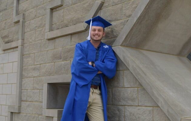 Matthew posing in cap and gown beside a stone UK statue
