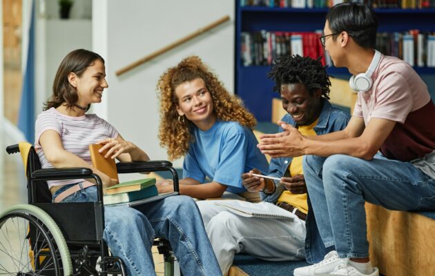 Group of 4 diverse teens sitting in a library and talking