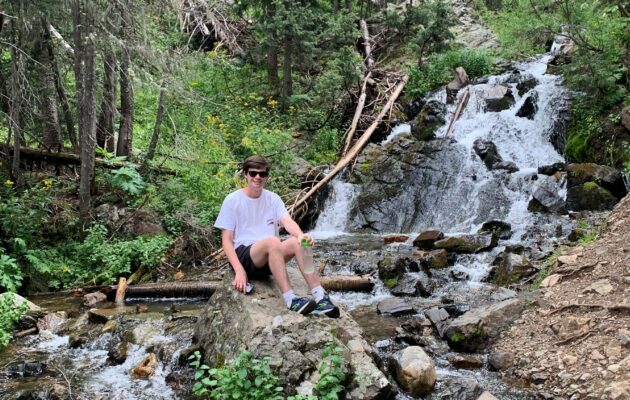 Weston sitton on a stone beside a small waterfall in a woodland setting