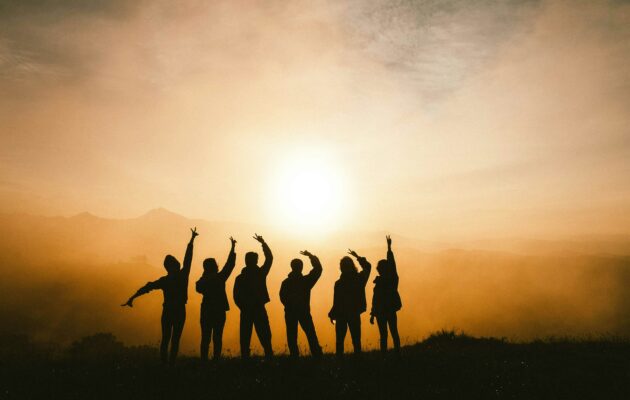 Silhouette of 6 people waving in front of a sunset