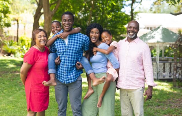 Multigenerational Black family with grandparents, parents, and two children, standing in a garden or park and smiling