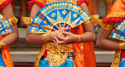 Young women in brightly colored outfits hold ornate fans for a dance performance
